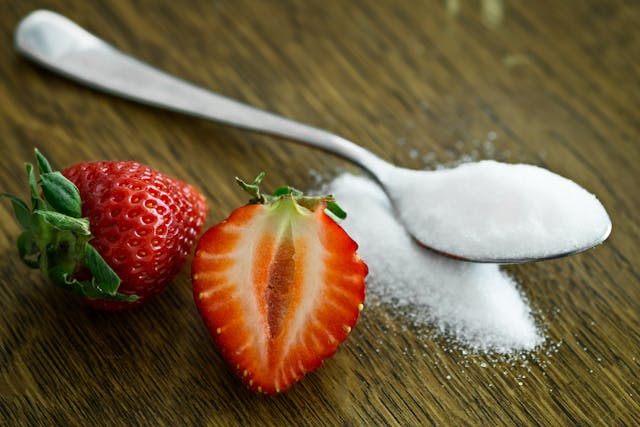 Granulated sugar and a ripe strawberry displayed side by side, prompting the question: "Is sugar vegan?"