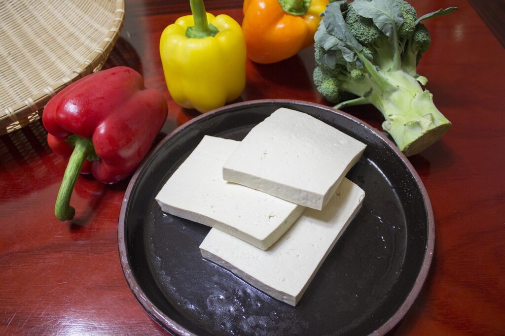 Tofu slices on a black plate with colorful vegetables in the background, representing a plant-based alternative for those asking, 