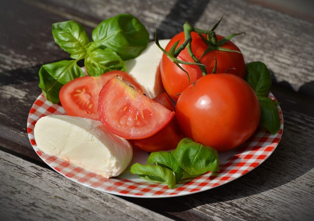 Fresh tomatoes, basil leaves, and slices of vegan mozzarella on a plate, addressing the question: 